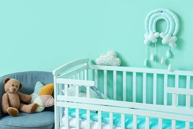 Çocuk odasının içinde turkuaz duvarın yanında beşik var.
