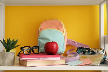 Okul çantası, kırtasiye, gözlük ve elma renkli duvarın yanında.