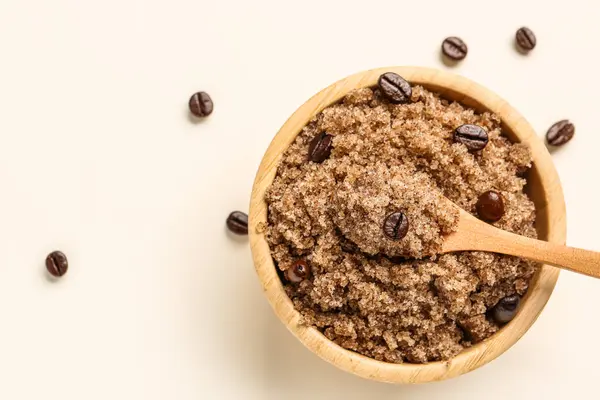 Bowl of body scrub and coffee beans on light background