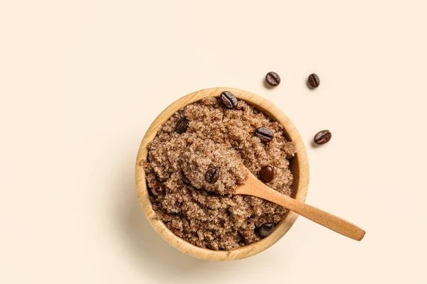 Bowl of body scrub and coffee beans on light background