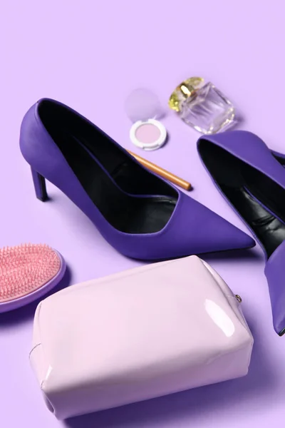 Stylish heels, cosmetics, bag and hair brush on lilac background, closeup