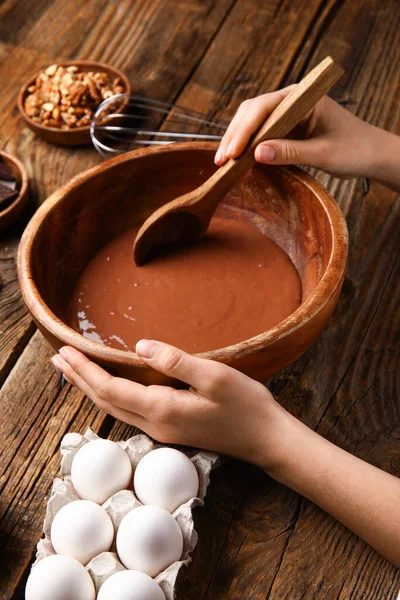 Woman preparing dough for chocolate brownie on wooden background