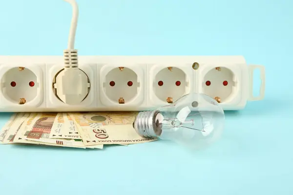 Power socket with plug, money and light bulb on blue background