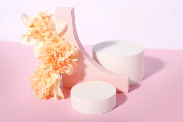Decorative plaster podiums with flowers on pink table against white background