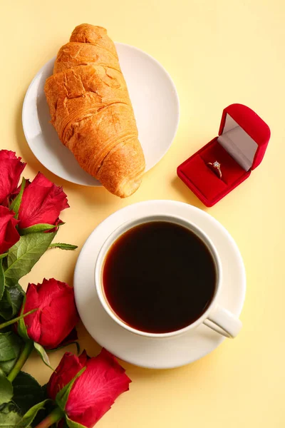 Box with engagement ring, croissant, coffee and roses on beige background