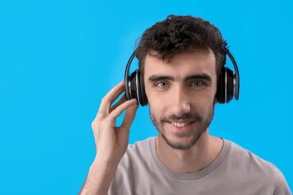 Junger Brünetter Mann Mit Kopfhörern Auf Blauem Hintergrund Nahaufnahme — Stockfoto