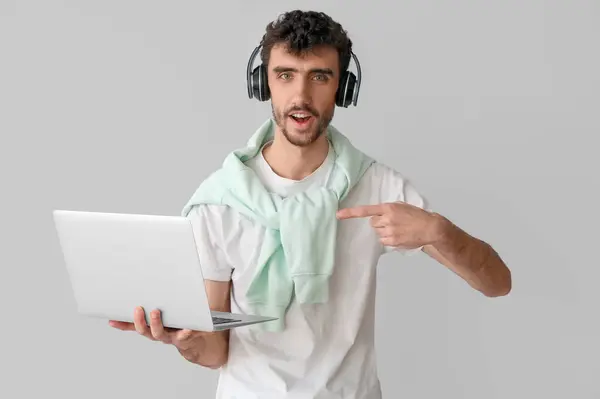 Молодий Чоловік Навушниках Вказує Ноутбук Світлому Фоні — стокове фото
