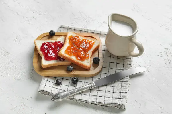 stock image Wooden board of tasty toasts with jams and milk in pitcher on grunge white background