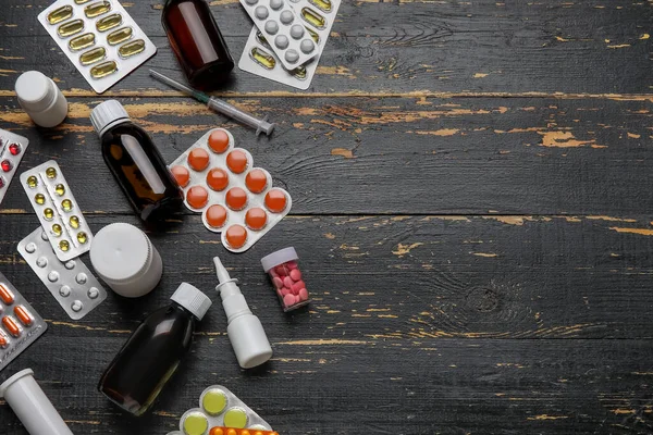 Different pills, syringe and bottles of medicines on black wooden background
