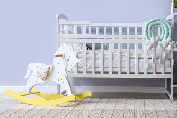 Interior of children\'s room with crib and rocking horse toy near white wall