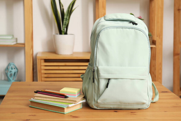 Stylish school backpack with stationery on wooden table in living room