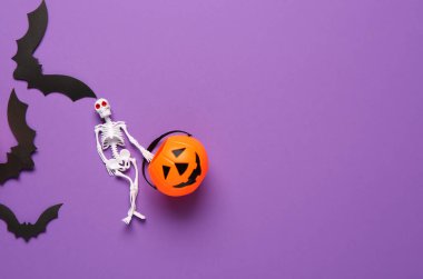 İskelet, balkabağı ve kağıt yarasalarla Cadılar Bayramı kutlamaları için mor arka planda kompozisyon