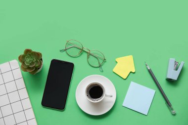 Telefon, kahve ve yeşil arka planda kırtasiye malzemeleri.