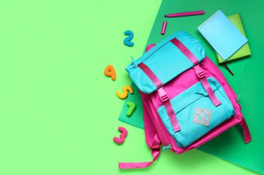 Şık okul çantası ve yeşil arka planda farklı kırtasiye malzemeleri