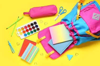 Şık okul çantalı kompozisyon ve sarı arka planda farklı kırtasiye malzemesi.