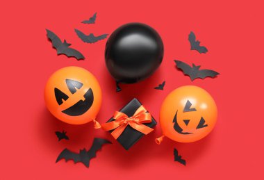 Farklı komik Cadılar Bayramı balonları hediye paketi ve kırmızı arka planda kağıt yarasalar.