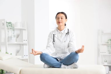 Kadın Asyalı doktor klinikteki kanepede meditasyon yapıyor.