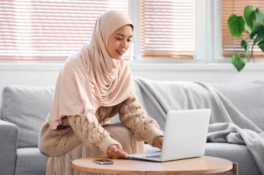 Genç Müslüman kadın evde dizüstü bilgisayar kullanıyor.