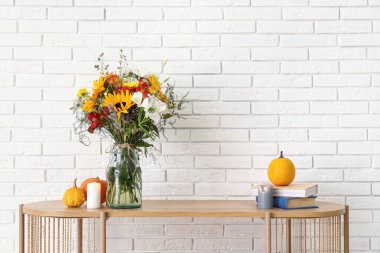 Raflarda bir buket sonbahar çiçeği ve beyaz tuğla duvarın yanında dekor var.
