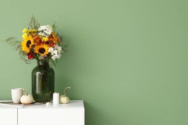 Sonbahar çiçekleri, yanan mumlar ve yeşil duvarın yanında balkabakları olan beyaz büfe.