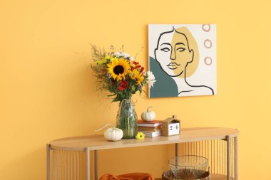 Sonbahar çiçekleri, balkabakları ve turuncu duvarın yanında dekoru olan ahşap raf ünitesi.