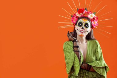 Cadılar Bayramı için turuncu arka planda giyinmiş düşünceli genç bir kadın.