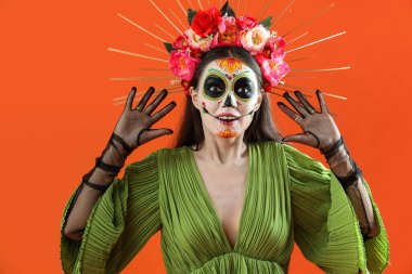 Cadılar Bayramı için turuncu arka planda giyinmiş genç bir kadın.