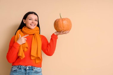 Bej arka planda balkabağını gösteren güzel bir kadın.