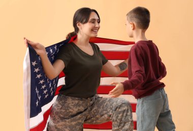 Bej arka planda Amerikan bayrağı olan küçük bir çocuk ve askeri annesi. Gaziler Günü kutlamaları