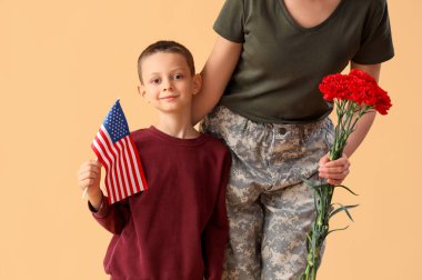 Amerikan bayrağı taşıyan küçük bir çocuk ve bej arka planda askeri annesi. Gaziler Günü kutlamaları