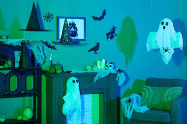 Cadılar Bayramı için dekore edilmiş karanlık oturma odasının içinde koltuk ve şömine rafı var.