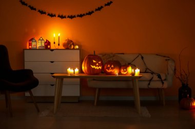 Cadılar Bayramı balkabakları ve yanan mumlarla dolu karanlık oturma odasının içinde.