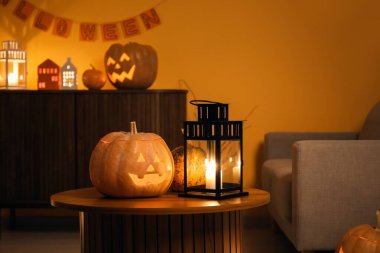 Karanlık oturma odasındaki masada yanan mumlarla Cadılar Bayramı balkabakları