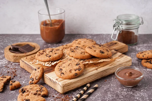 Wooden board of tasty cookies with chocolate chips and sauce on table