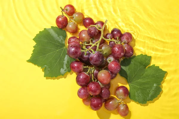 Lekkere Rijpe Druiven Met Bladeren Water Gele Achtergrond — Stockfoto