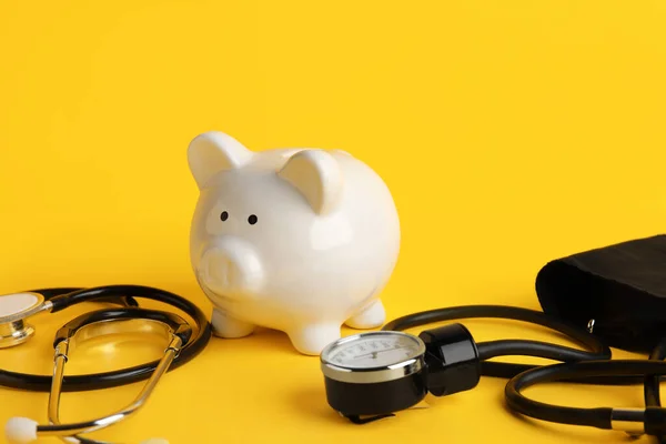 Piggy bank with stethoscope and tonometer on yellow background