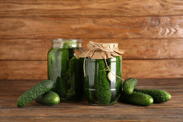 Jars with canned cucumbers and fresh vegetables on wooden background