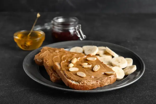 Plate of toasts with peanut butter and banana on black background