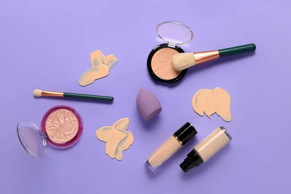 Bottles of makeup foundation with samples and decorative cosmetics on purple background