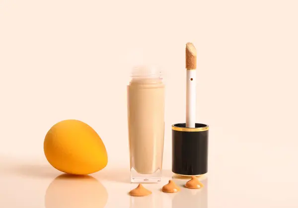Bottle of makeup foundation and sponge on yellow background