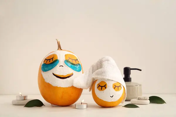Pumpkins with masks and spa supplies on light background