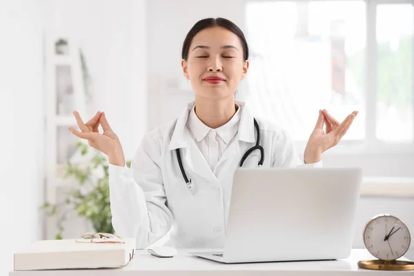 Female Asian doctor meditating at table in clinic
