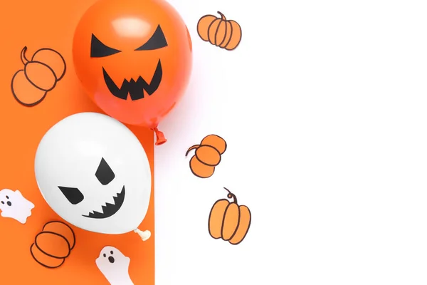 Different funny Halloween balloons with paper ghosts and pumpkins on colorful background