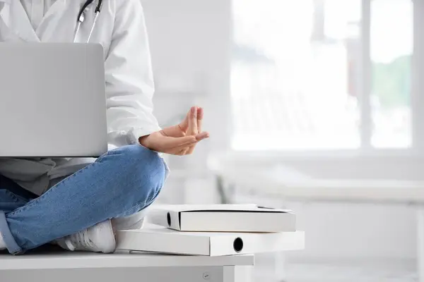 Female doctor with laptop meditating on table in clinic, closeup