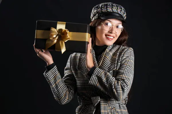 Young Asian woman with gift on dark background. Black Friday sale