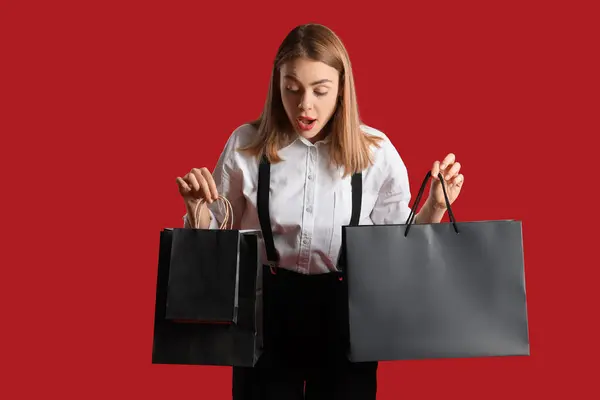 Σοκαρισμένη Νεαρή Γυναίκα Τσάντες Για Ψώνια Κόκκινο Φόντο Μαύρη Παρασκευή — Φωτογραφία Αρχείου