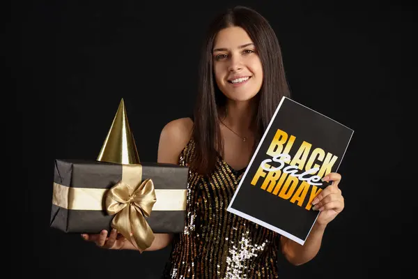 Young woman with gift and party hat on dark background. Black Friday sale
