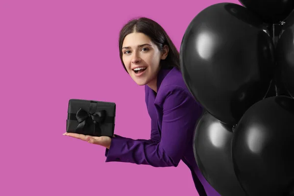 Young woman with gift box and balloons on purple background. Black Friday sale