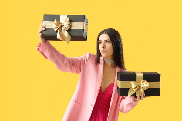 Thoughtful young woman with gifts on yellow background. Black Friday sale