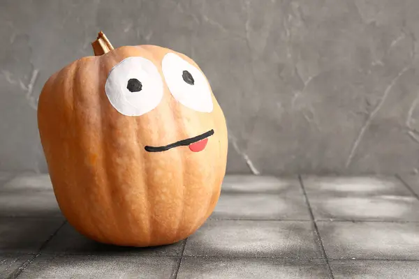 Funny Halloween pumpkin with drawn face on grey tiled table